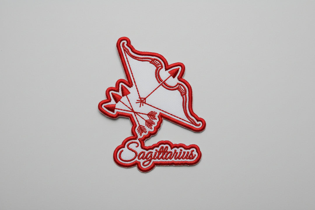 Red Sagittarius archer bow-and-arrow zodiac embroidered patch with “Sagittarius” script text on a white grid background.