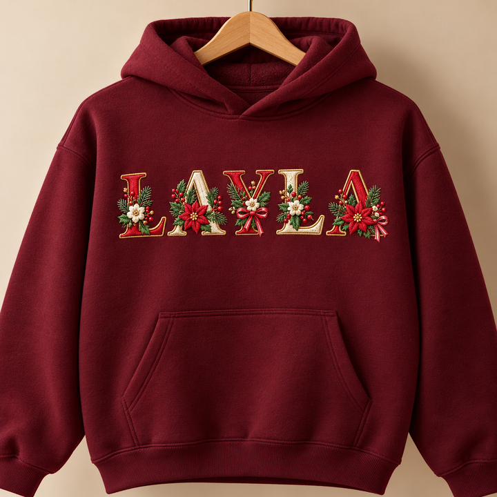 Festive Poinsettia Alphabet custom name "LAYLA" machine embroidered on a burgundy hoodie – red and cream serif letters with gold outline, poinsettias, holly and berries | Hand Finished in Dubai | EmbroMania