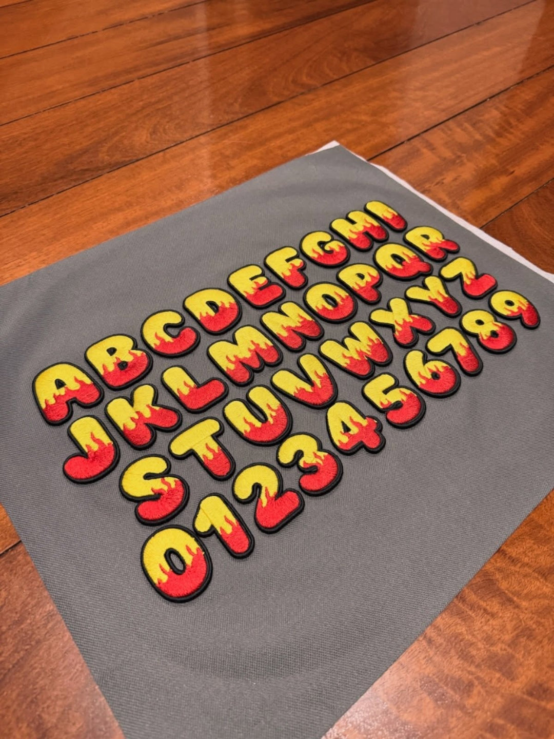 Inferno Pop Custom Cap Font reference sheet – full A–Z and 0–9 flame bubble letters · Yellow fill · Red flame · Black outline | Hand Finished in Dubai | EmbroMania