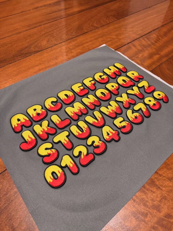 Inferno Pop Custom Cap Font reference sheet – full A–Z and 0–9 flame bubble letters · Yellow fill · Red flame · Black outline | Hand Finished in Dubai | EmbroMania